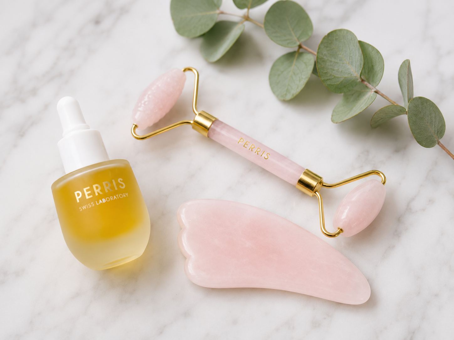Ein Gesichtssöl von Perris Swiss Laboratory neben einem passenden Rosenquarz-Roller und einem Gua-Sha-Stein auf hellem Marmor.