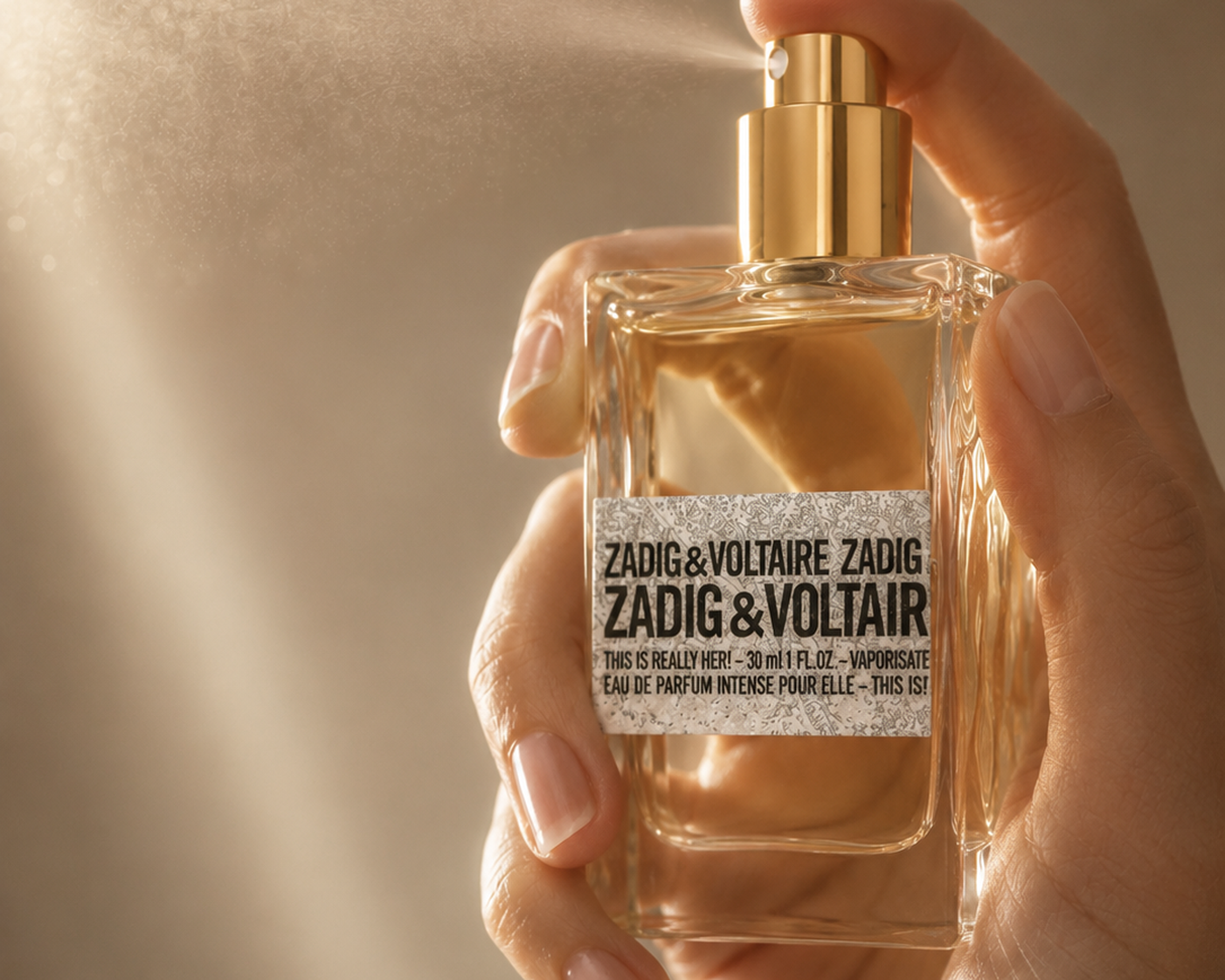 Hand sprüht Zadig & Voltaire This is Really Her! Eau de Parfum Intense aus dem Flakon mit   goldenem Zerstäuber im warmen Gegenlicht