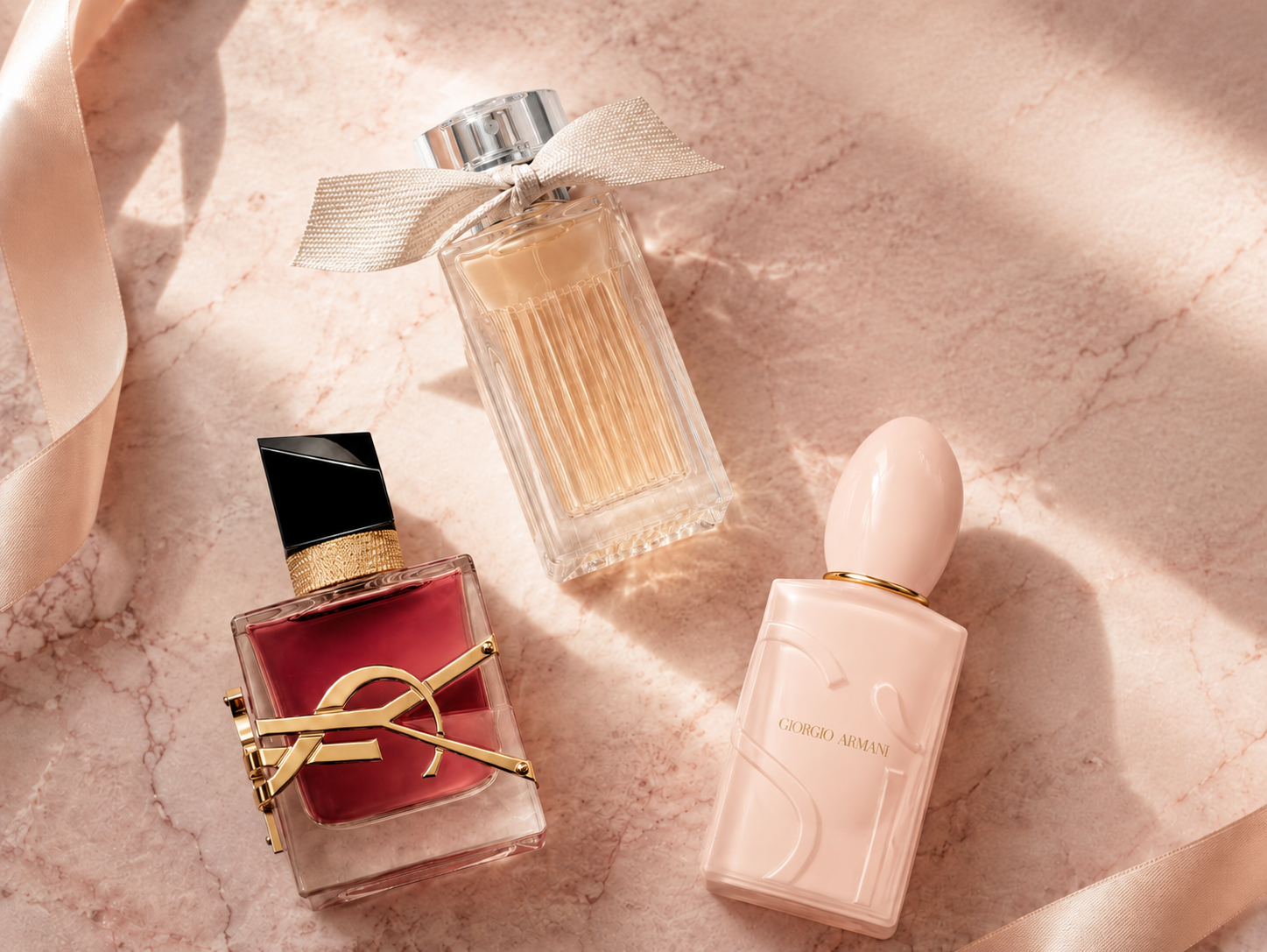 Flatlay mit Damenparfums auf rosa Marmor: YSL Libre, Giorgio Armani Si und ein Flakon mit   Satinschleife, dekoriert mit rosa Seidenband