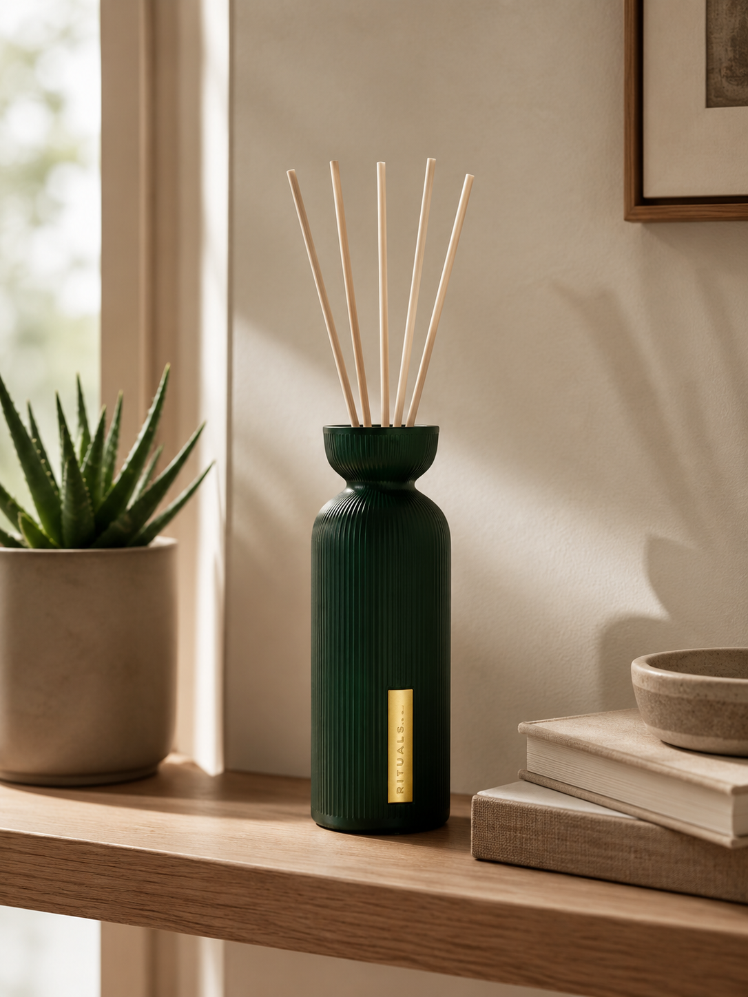 Rituals Diffuser in dunkelgrüner Riffelglasflasche mit Duftstäbchen auf einem Holzregal im   Sonnenlicht