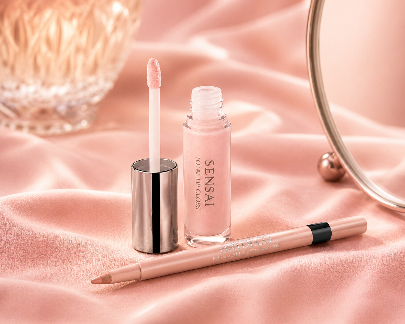 Produktfotografie eines geöffnetem Ligloss und eines Lipliners auf einem rosa Tuch