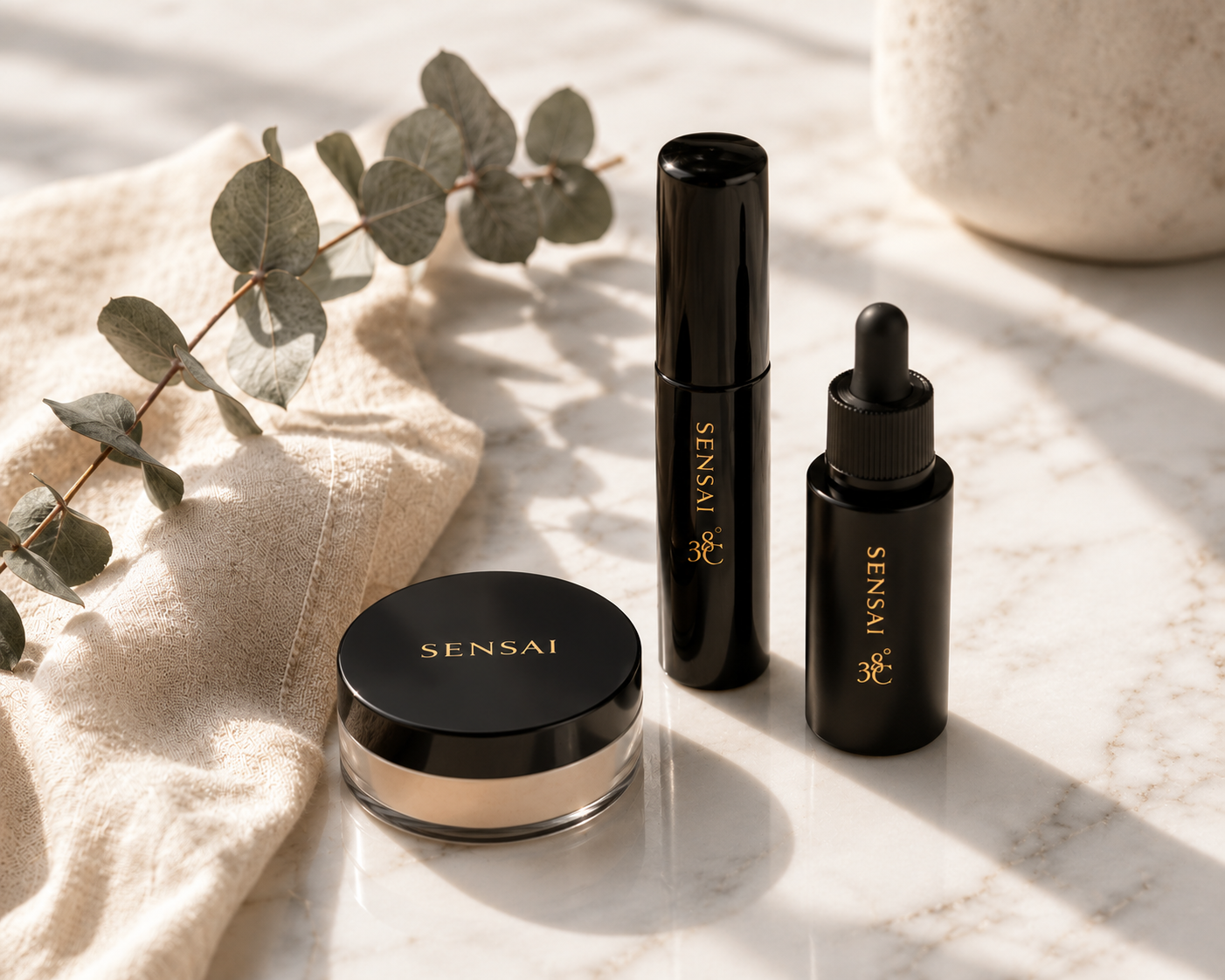 Sensai Make-up-Set mit losem Puder, Mascara und Serum auf hellem Marmor