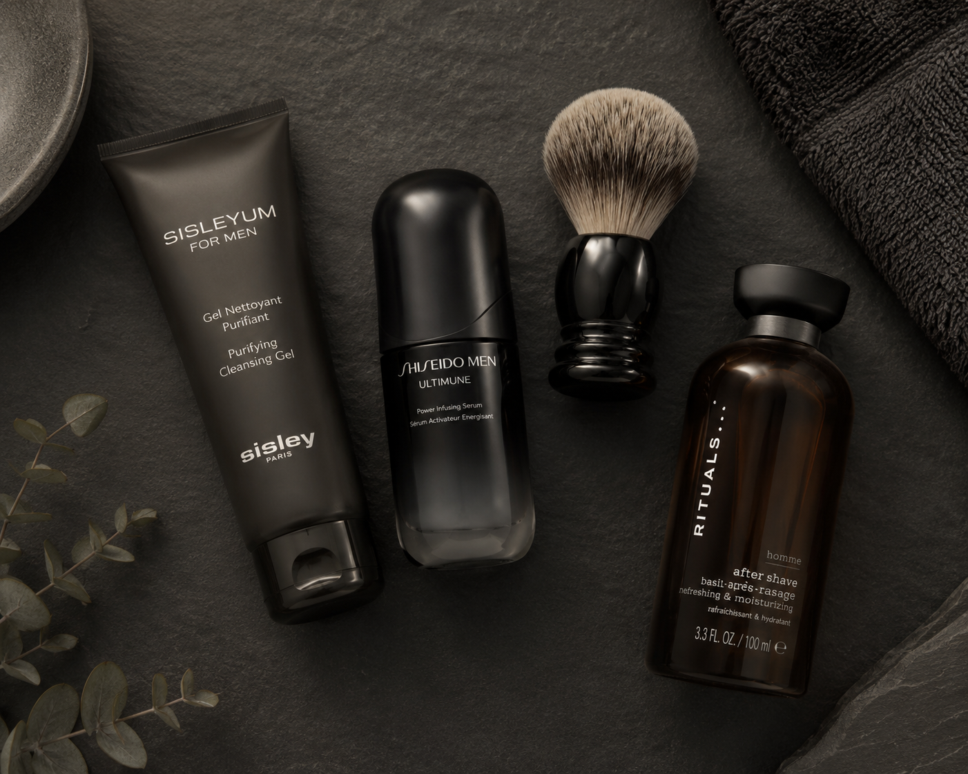 Männerpflege-Produkte auf dunklem Schiefer: Reinigungsgel, Serum, Rasierpinsel und After Shave