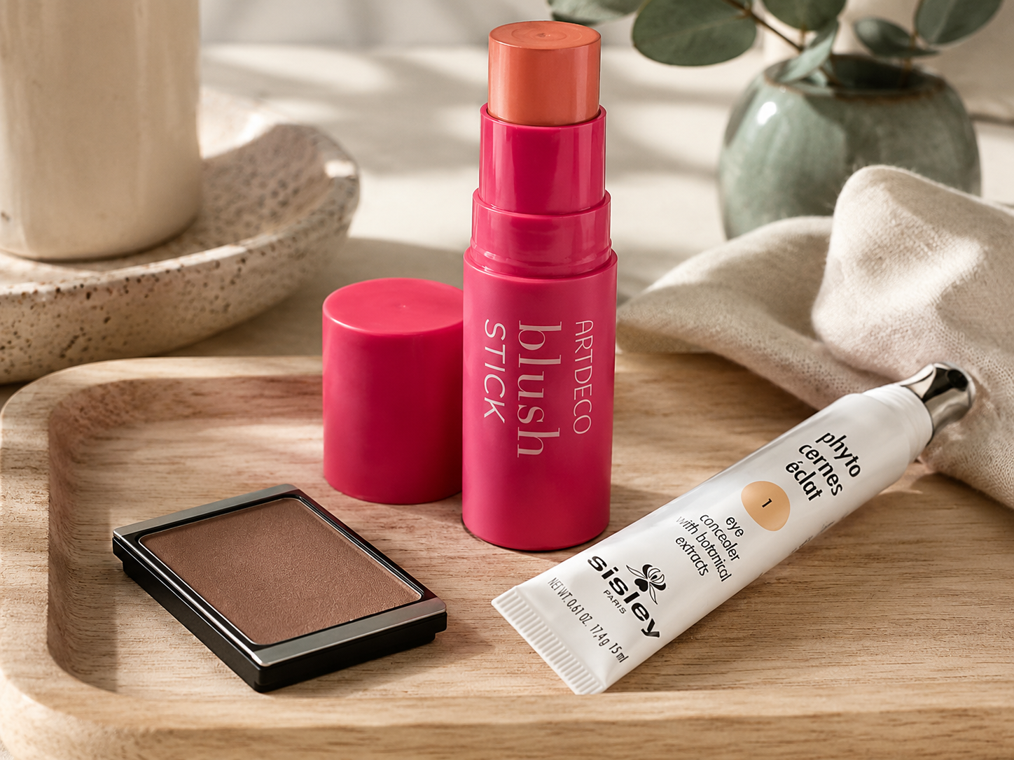 Nachhaltige Make-up Produkte auf einem Holzbrett neben einer Pflanze aufgestellt